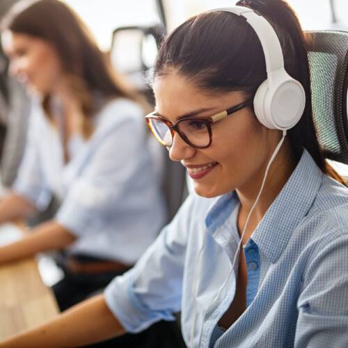 Friendly young woman helpline operator with headphones in call center